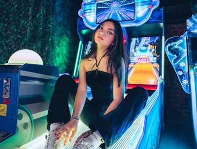 A person sitting on an arcade game machine platform with neon lights in the background. The arcade game is called 'Lane Master' and features a colorful design with bowling-themed imagery.