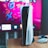 A gaming console is placed on a wooden table with a game controller nearby. In the background, a television screen displays colorful graphics, including geometric shapes and vibrant colors.