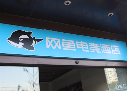 A building entrance features a vibrant blue sign with white Chinese characters and a stylized orca logo in black and white. The overall appearance suggests an establishment focused on eSports or digital activities.